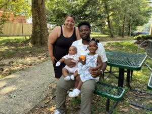 Staff member posing with smiling dad with an infant and toddler on his lap.