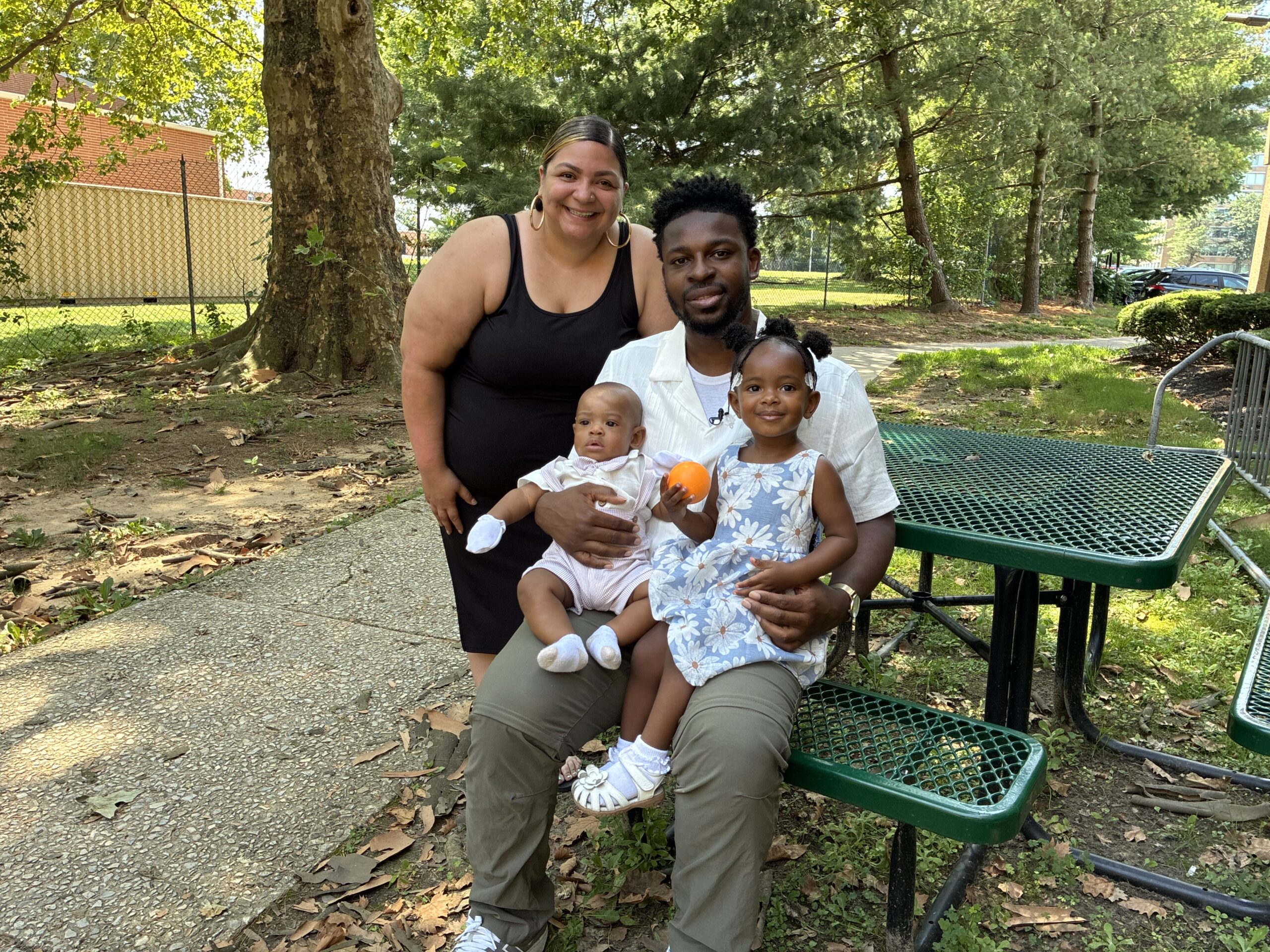 Staff member posing with smiling dad with an infant and toddler on his lap.