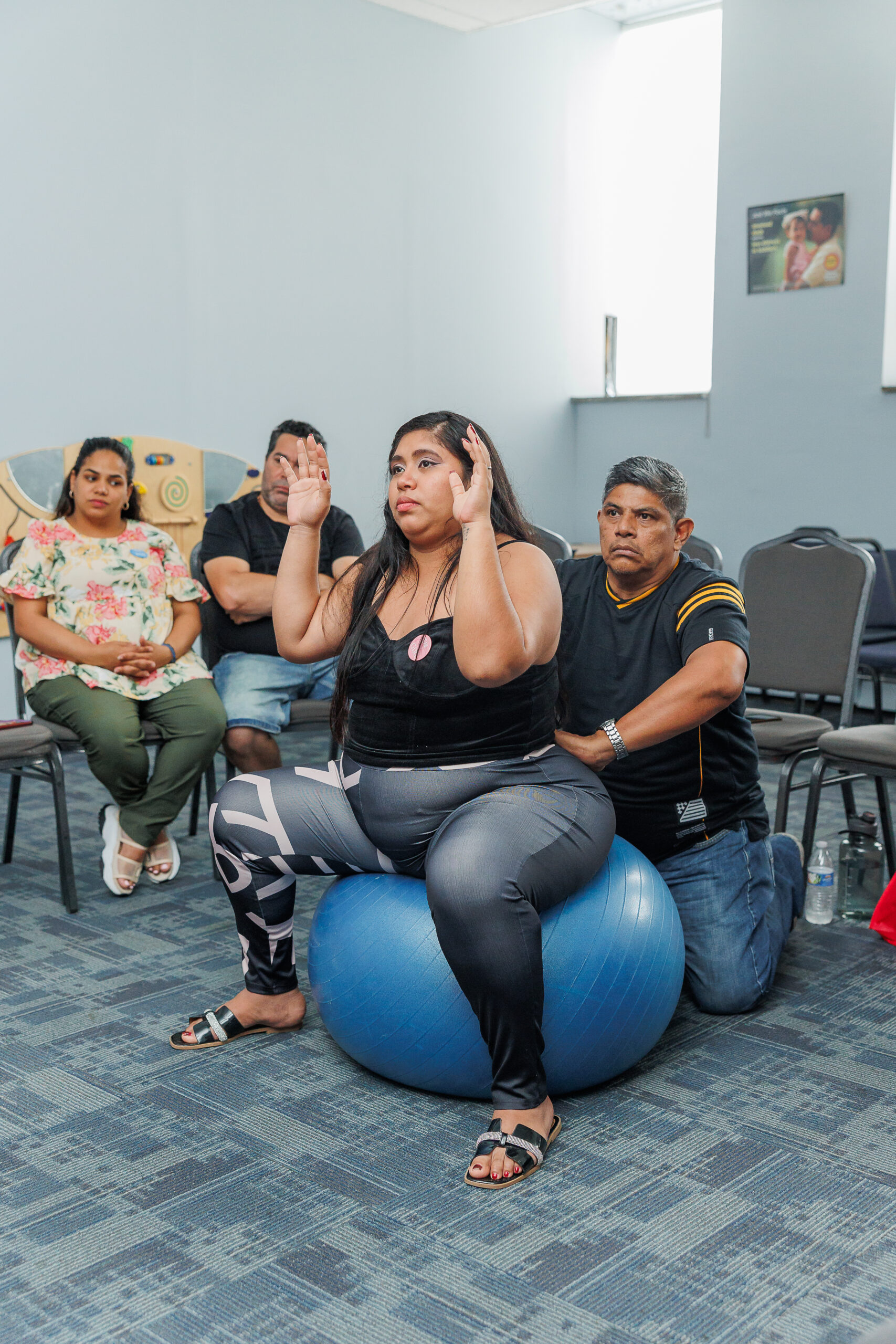 Pregnant mother being assisted by her partner while sitting on large medicine ball.